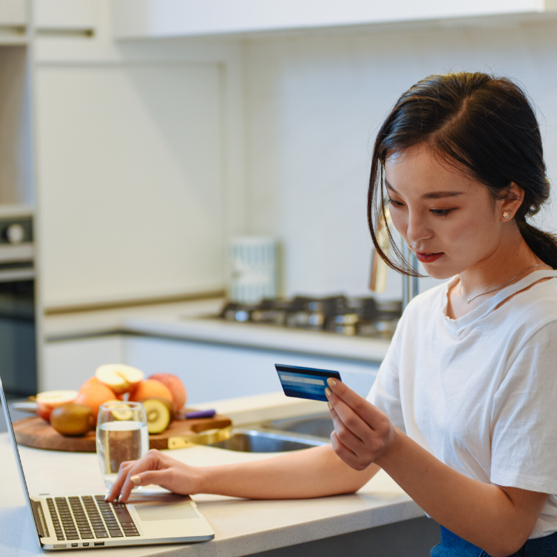 Woman online shopping on a laptop with credit card at her kitchen bench